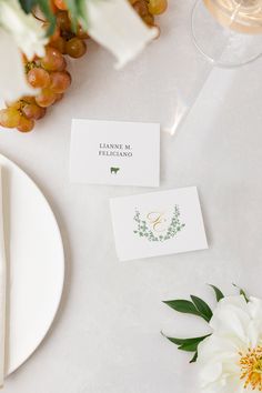 two place cards on a table with flowers and wine glasses next to them, along with a white flower