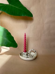 a pink candle sitting on top of a table next to a green plant