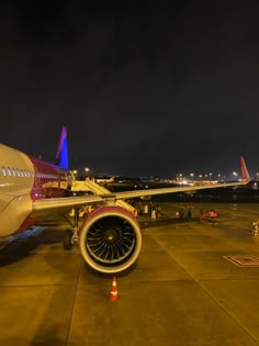 an airplane is parked on the tarmac at night with its lights on and people around it