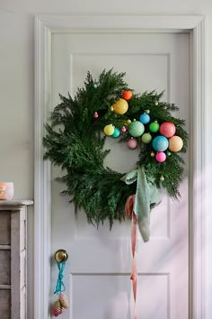 a wreath on the front door with ornaments hanging from it's hooks and ribbon