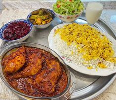 a silver tray topped with different types of food next to bowls of salad and rice