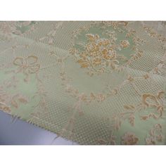 an image of a table cloth with flowers and leaves in gold on light green background