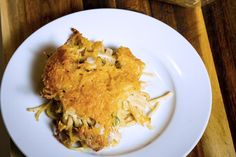 a white plate topped with pasta and cheese covered casserole on top of a wooden table