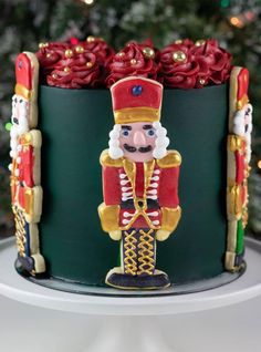 a decorated cake with a nutcracker and roses on the top is sitting in front of a christmas tree