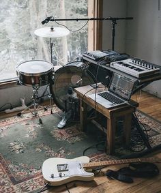 a room with guitars, drums and other musical equipment on the floor in front of a window