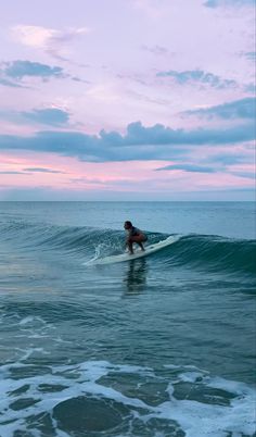 a person riding a surfboard on top of a wave in the ocean at sunset