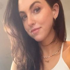 a woman with long hair wearing a white tank top and gold chain choker necklace