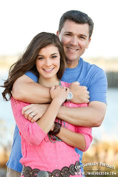 a man and woman hugging each other in front of water