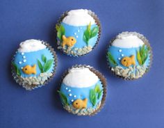 four cupcakes decorated with fish and seaweed in blue frosting on a blue background