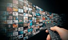 a hand holding a remote control in front of a wall of pictures