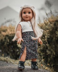 a doll with blonde hair wearing a dress and black boots standing in front of bushes