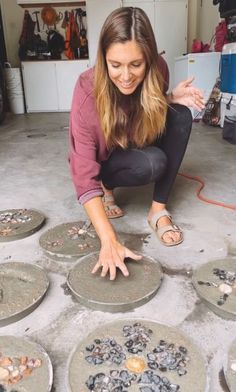 a woman kneeling down on the ground in front of several plates with shells all over them