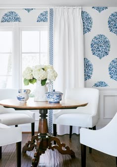 a dining room table with white chairs and blue and white wallpaper on the walls