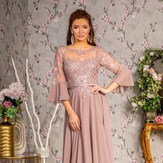 a woman standing in front of a floral wallpaper wearing a dress with bell sleeves