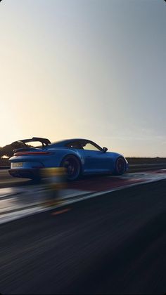 a blue sports car driving on a race track at sunset or dawn with the sun behind it