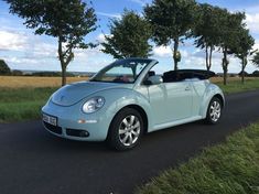 a blue convertible car parked on the side of a road next to trees and grass