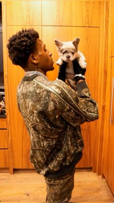 a man holding a small dog in his arms while standing next to a kitchen counter