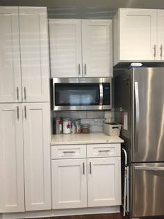 a kitchen with white cabinets and stainless steel appliances, including a microwave on the wall