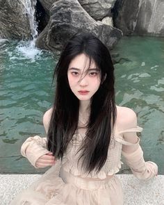 a woman with long black hair standing in front of water