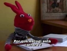 a red stuffed animal sitting on top of a desk next to an open book with the caption por que escogi est carra?