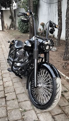 a black motorcycle parked next to a tree on a brick walkway in front of a house