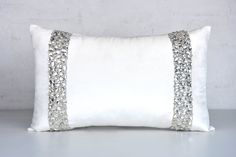 a white pillow with silver sequins on the front and sides, sitting against a gray wall