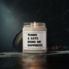 a candle that says tennis and cats bring me happiness on the front with a black background