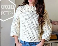 a woman wearing a white crochet sweater standing in front of a bed with her hands on her hips