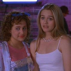 two young women standing next to each other in front of a brick wall and neon sign