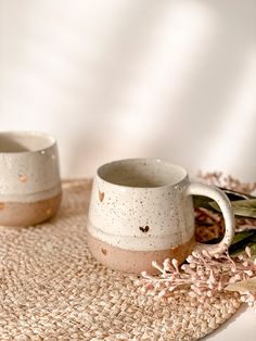 two mugs sitting next to each other on top of a place mat with pink flowers