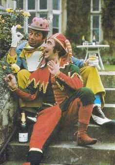 two men dressed as clowns sitting on steps next to each other and one holding a bottle