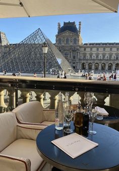 two chairs and a table with wine glasses on it in front of a pyramid shaped building