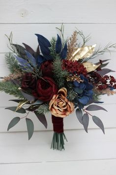 a bridal bouquet with red, orange and blue flowers on white wood planks