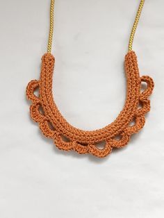 an orange crocheted necklace is hanging from a gold chain