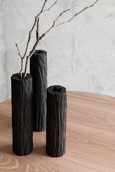 three black vases sitting on top of a wooden table next to a tree branch