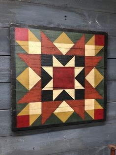 a wooden wall hanging on the side of a building with an abstract quilt design in red, yellow and green