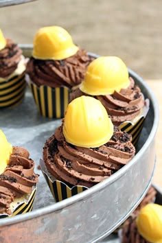 cupcakes with chocolate frosting and yellow candies on top in a metal tray