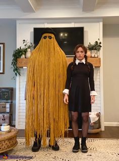 a woman standing next to a giant yellow monster costume in a living room with a fireplace