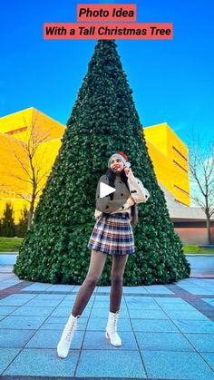 a woman standing in front of a christmas tree with her hands on her hips and the words photo idea with a tall christmas tree behind her