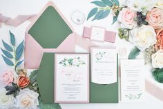 the wedding stationery is laid out with flowers and greenery on it, including roses