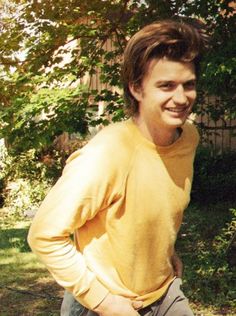 a young man standing in front of a tree with his hands on his hips and smiling