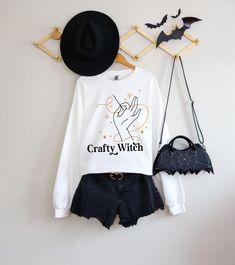 a white shirt with the words crafty witch written on it next to a black purse