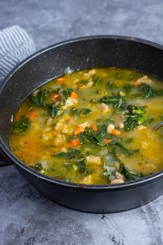 a pot filled with soup and vegetables on top of a gray countertop next to a towel