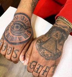 two hands with tattoos on them, one has an all seeing eye and the other has roman numerals