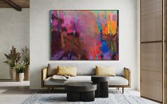 an abstract painting hangs on the wall above a couch and coffee table in a modern living room