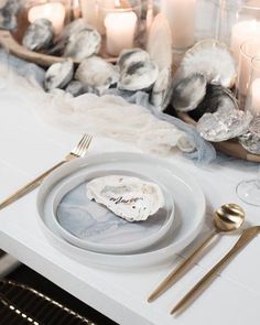 a white table topped with plates and silverware next to candlelight candles on top of a counter