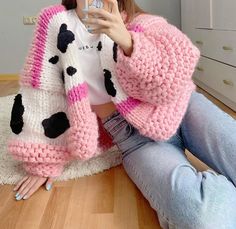 a woman sitting on the floor taking a selfie with her cell phone wearing a cow sweater