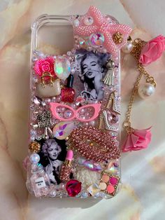 an iphone case with pink accessories and pearls on the back, sitting on a marble surface