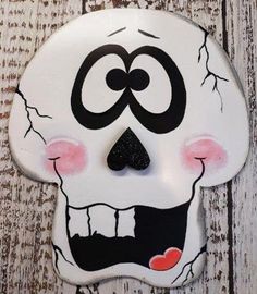 a white skull with black eyes and mouth painted on it's face, sitting on a wooden surface