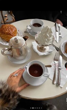 a table topped with plates of food and cups of coffee next to each other on top of a white table